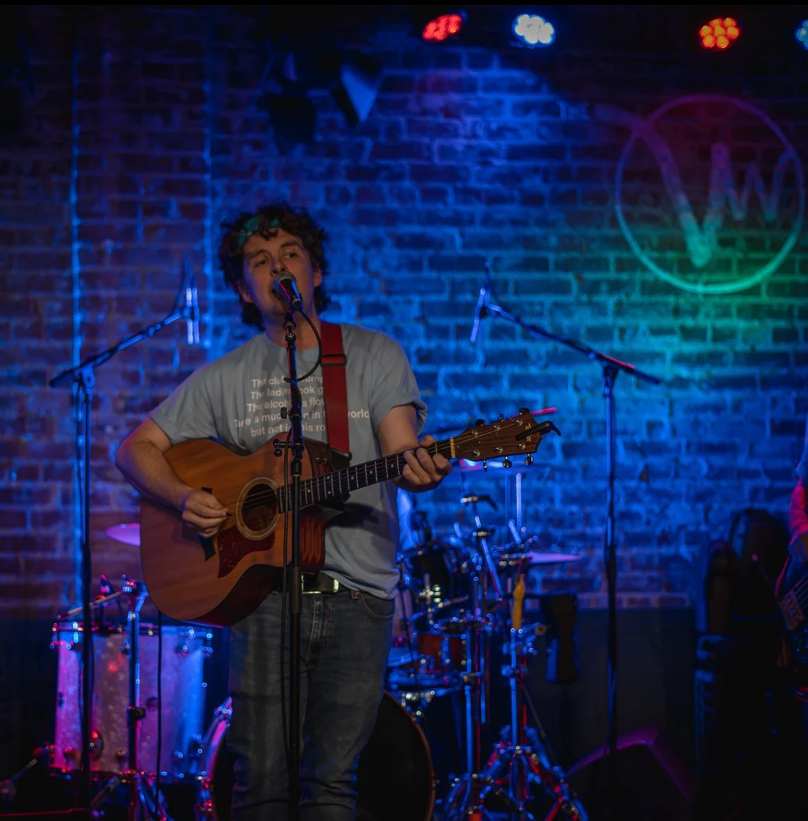 Matt Tuley performing on a blue-lit stage against a brick wall