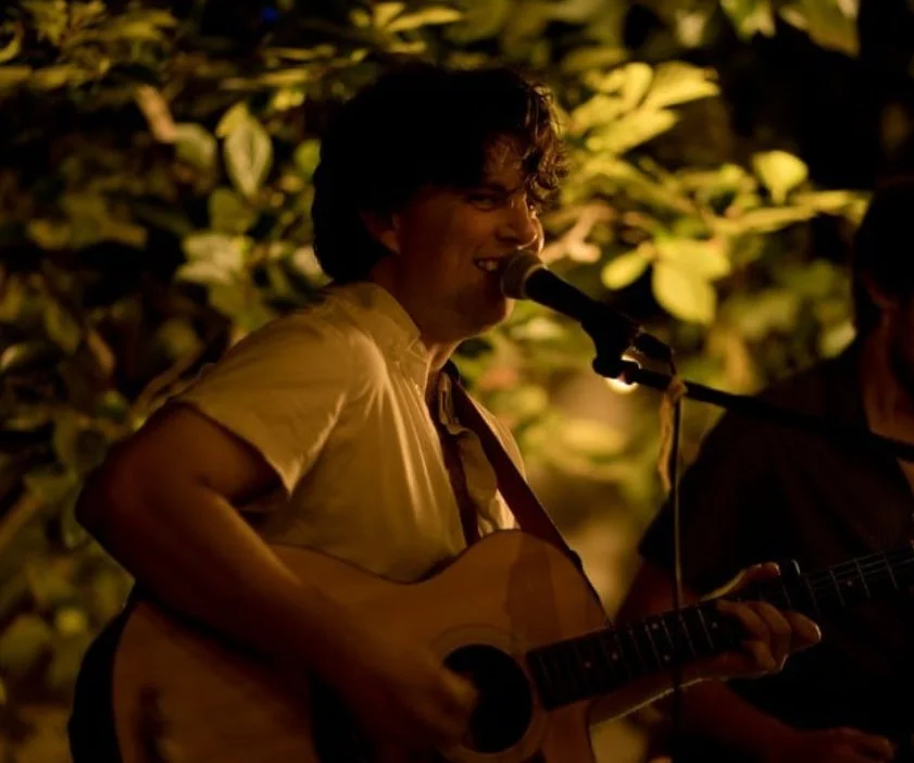 Matt Tuley playing acoustic guitar at an outdoor evening celebration