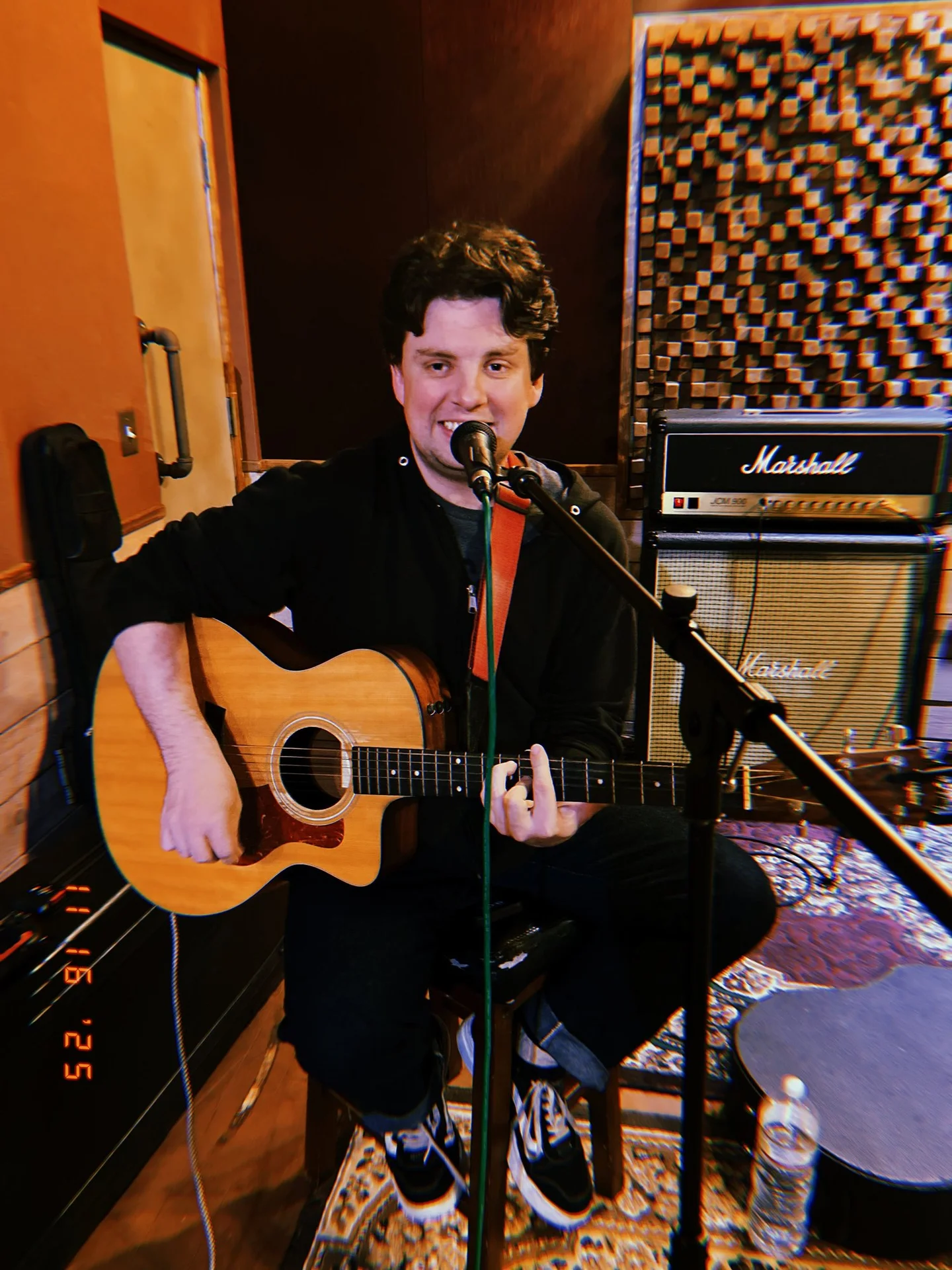 Matt Tuley singing and playing acoustic guitar in a warmly lit recording studio