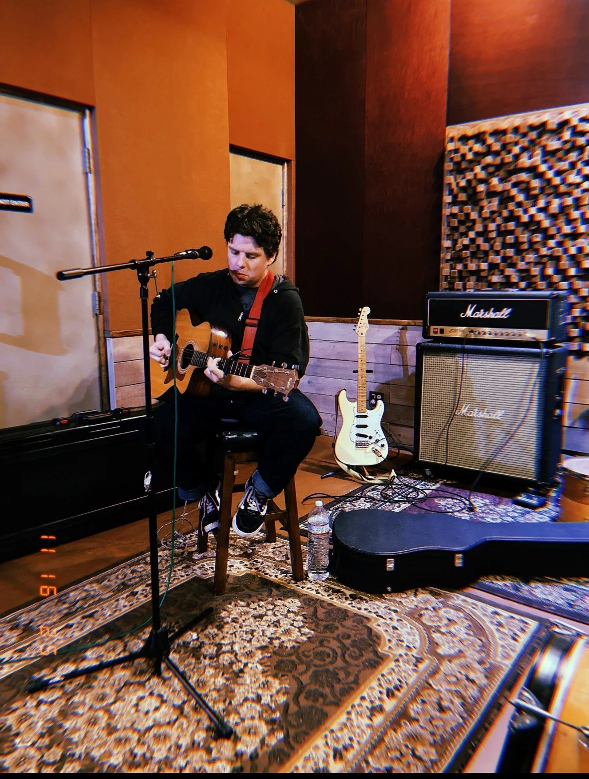 Matt Tuley recording with his acoustic guitar among studio amplifiers